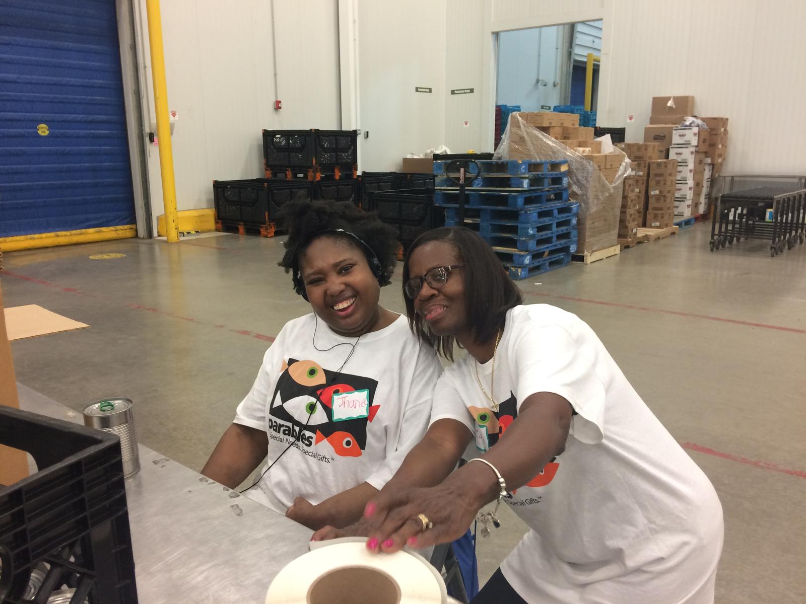 two black young adults in matching shirts smile while packing boxes.