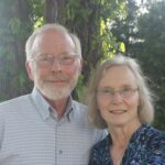 an elderly white man and an elderly white woman pose under a tree
