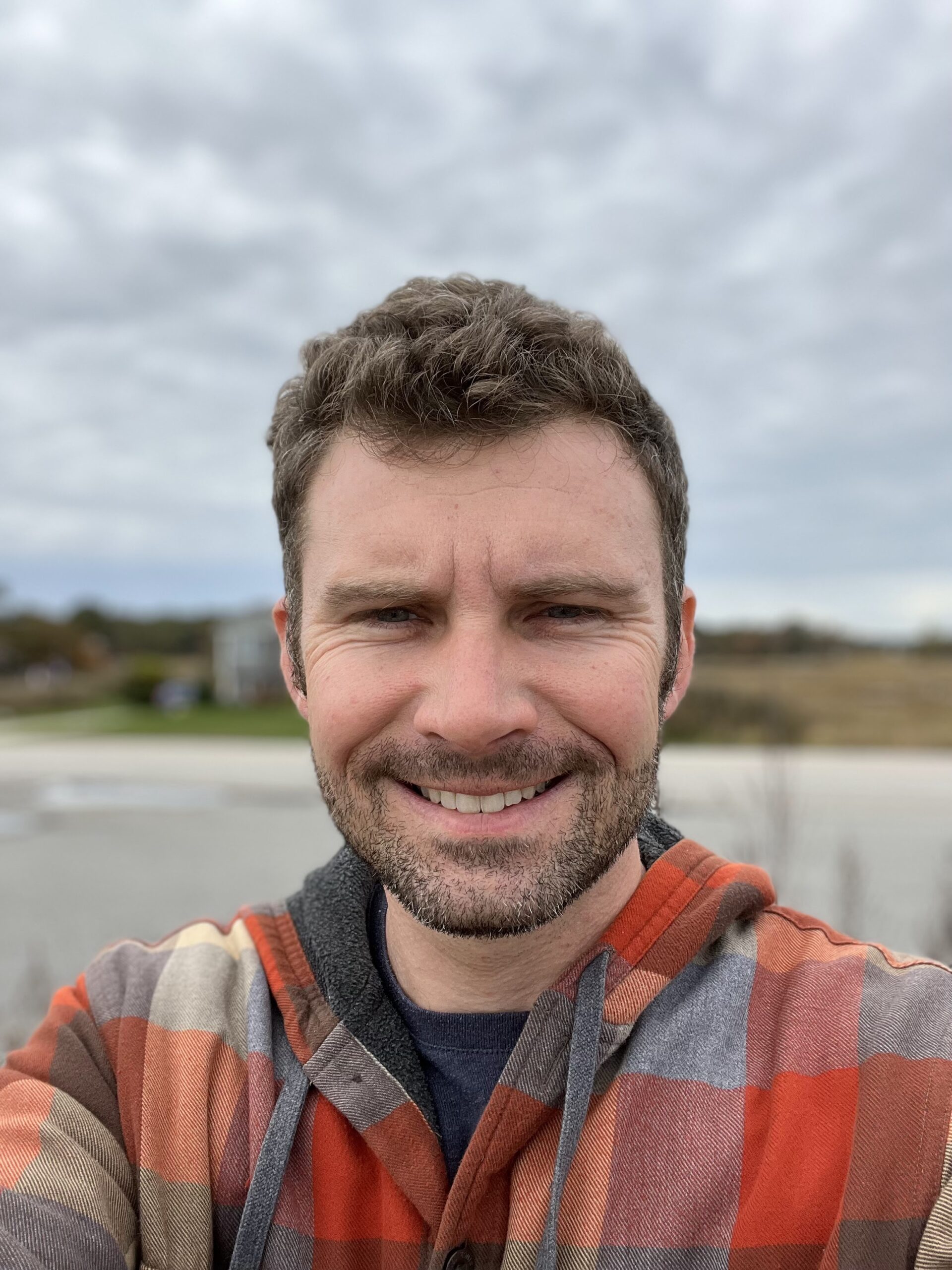 Steve is a young adult white man wearing a flannel shirt with a neatly trimmed brown beard.