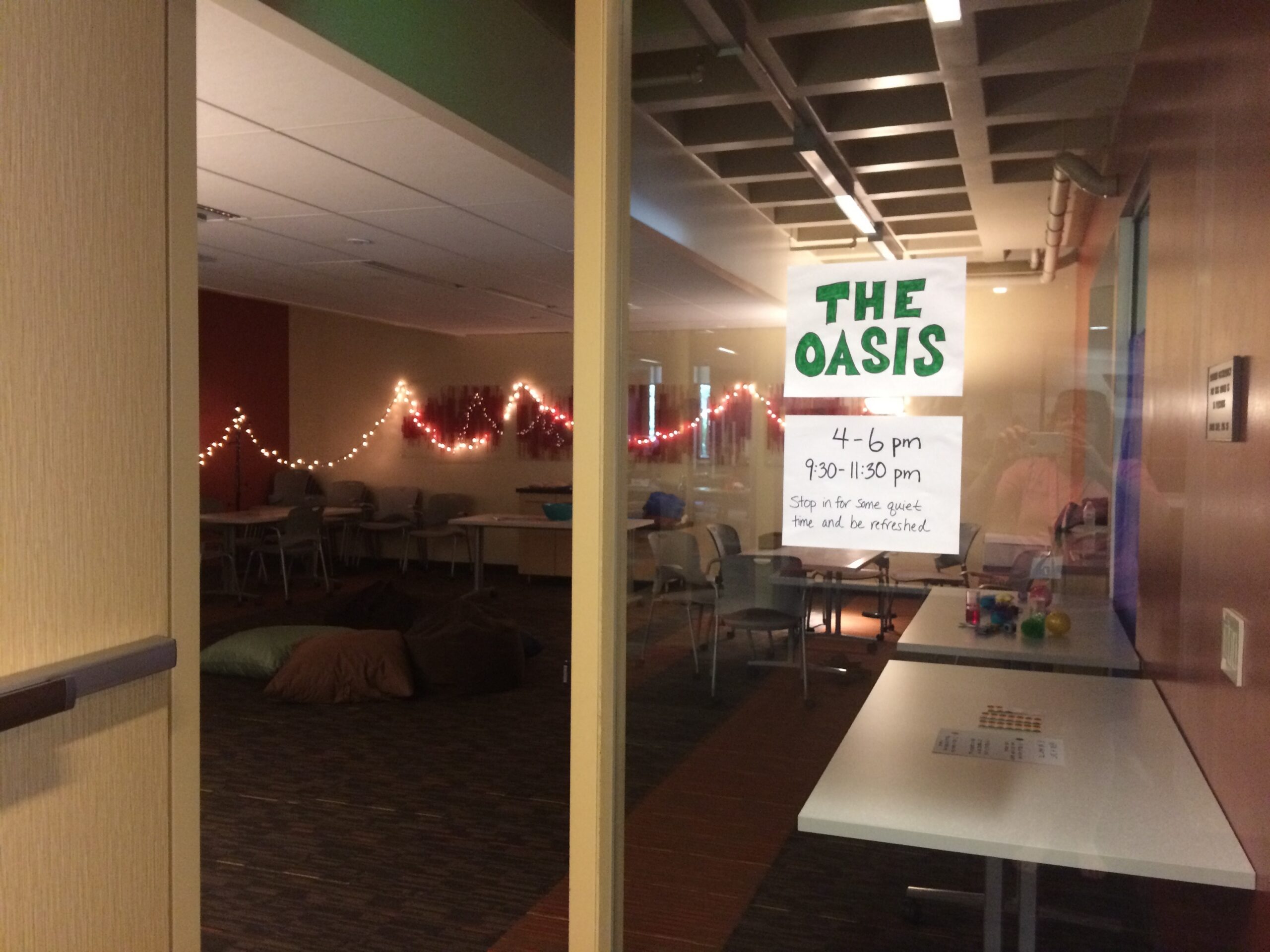 a darkened room lit by twinkle lights. the floors are lined with big pillows and tables hold coloring books, puzzles, and fidgets.