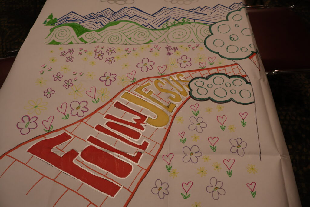 a large piece of paper with a color drawing that says follow Jesus with hearts and flowers in the foreground and mountains in the background