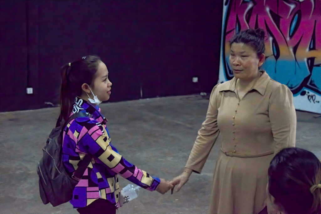 Two women shake hands in front of a black wall