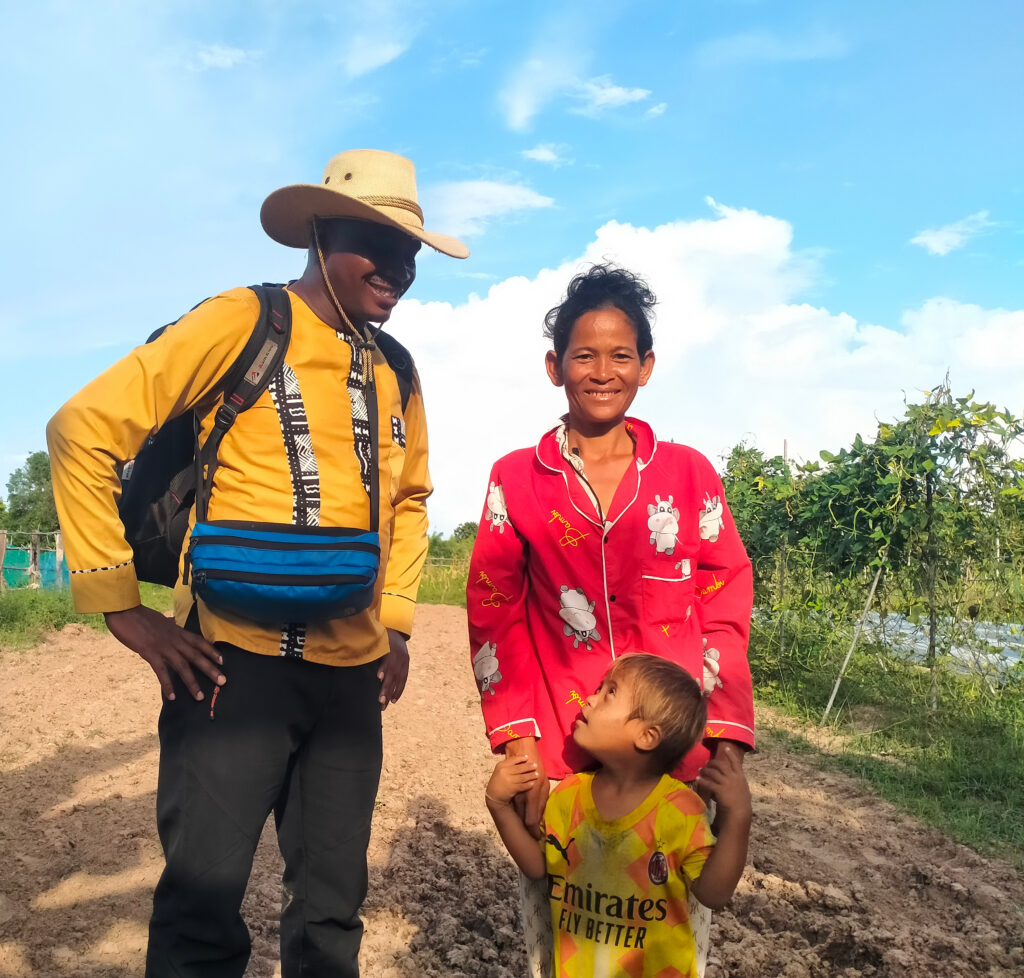 A man in a cowboy hat and a yellow shirt smiles down on a mother in a red shirt and a boy with down syndrome in a yellow soccer jersey.