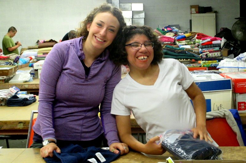 Two smiling young women sort materials in warehouse