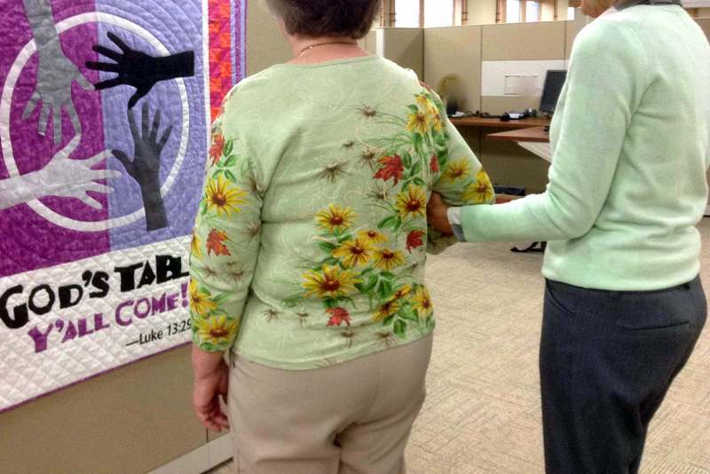 two women standing in a church hallway, one of them is holding the elbow of the other one