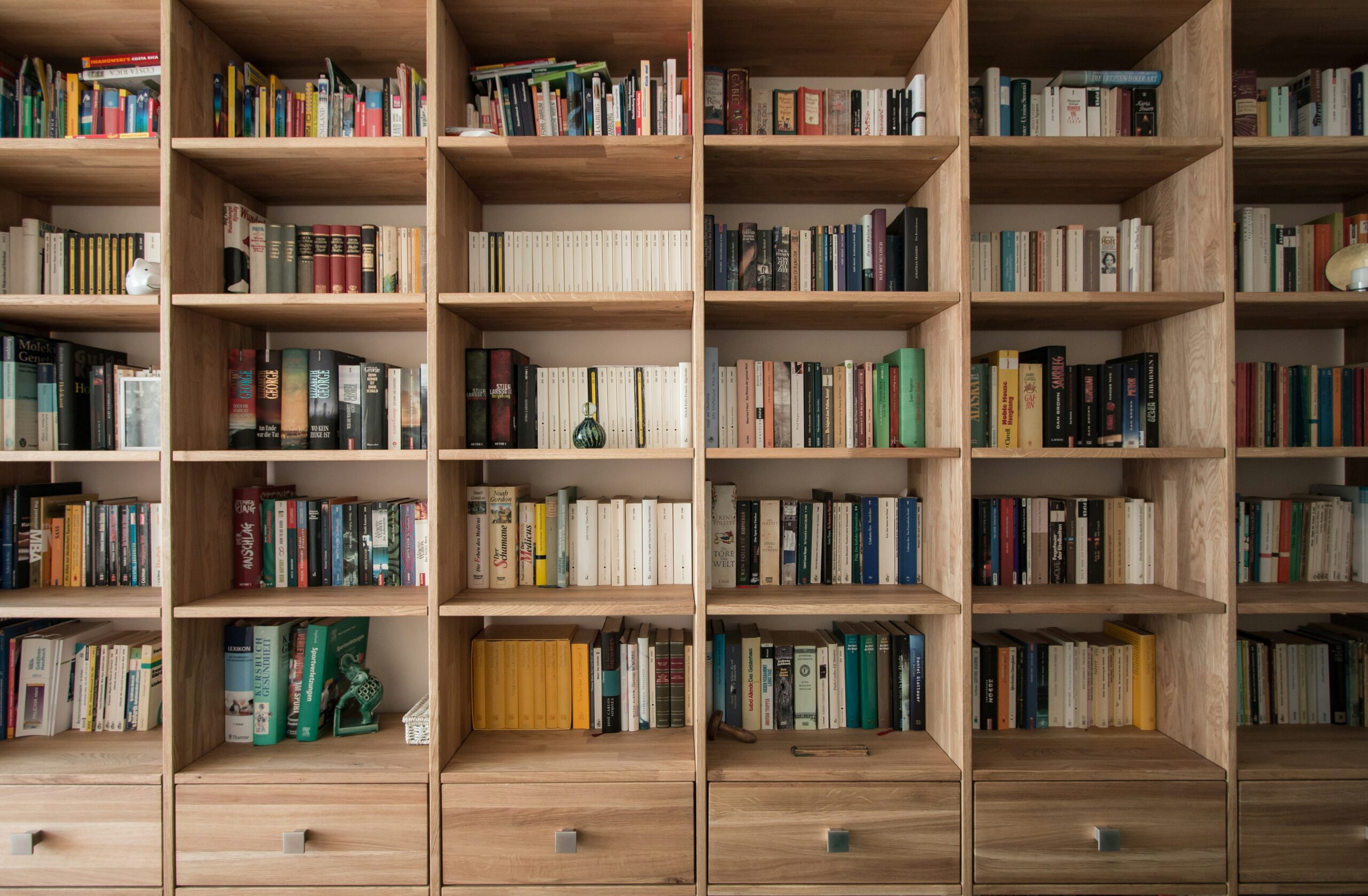 a bookshelf that takes up the entire wall, made of light brown wood, filled with books of different colors
