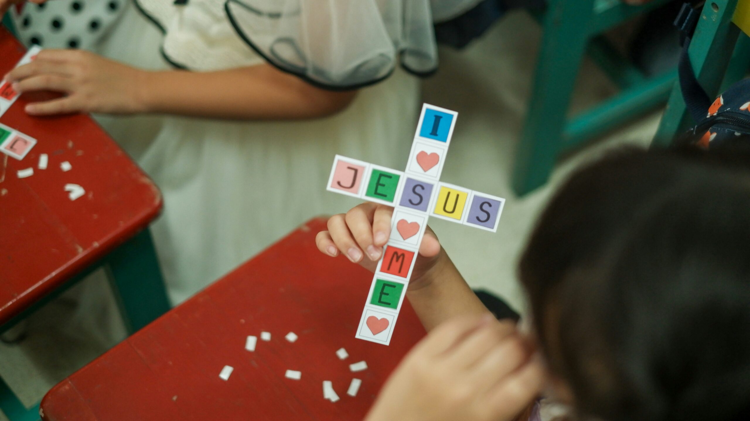 a child holds a paper cross that says Jesus loves me